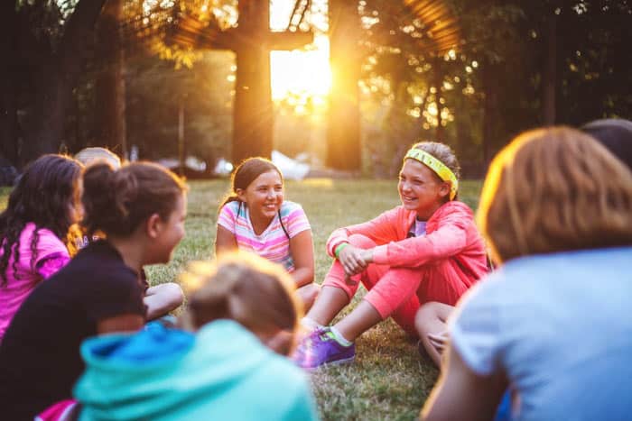 A group of Youth girls smiling and talking to one another on a lawn with a cross behind them